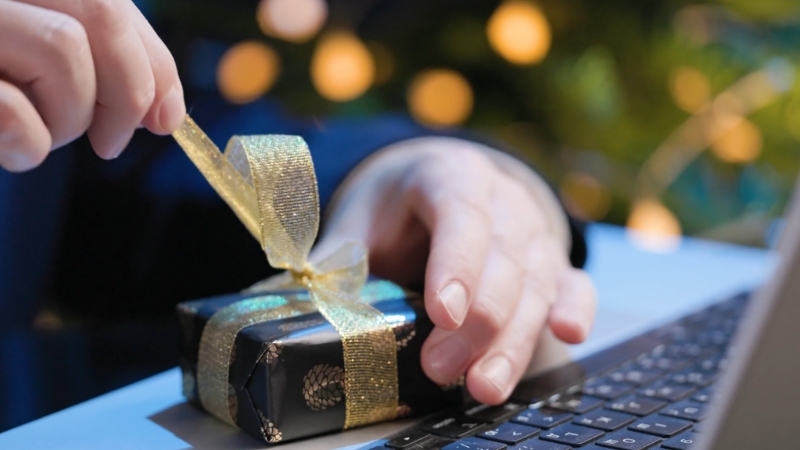 Person opening a small wrapped box at a laptop as part of corporate gift ideas for clients and business partners