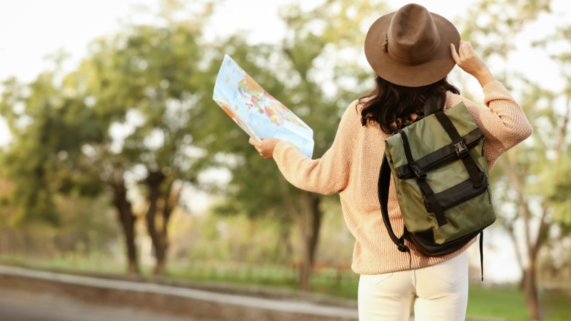 Woman with a backpack holding a map outdoors as an example of travel and outdoor corporate gift ideas