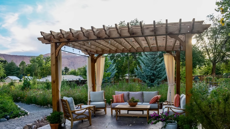 Pergola with outdoor seating and curtains creating a private lounge area in a landscaped backyard