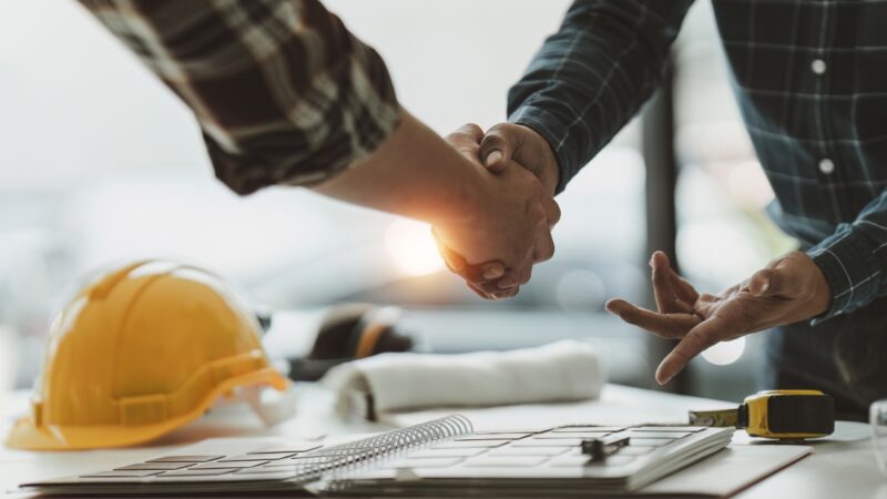 Two construction professionals shake hands over project plans during permit coordination